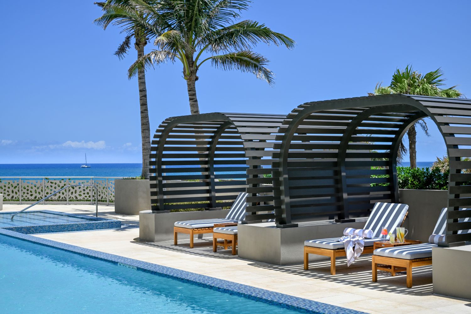 Elegant cabanas beside a pool overlook the ocean, surrounded by palm trees and bright blue skies at Amrit Ocean Resort.