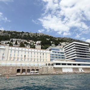Hotel Excelsior Dubrovnik overlooking the Adriatic Sea, with a backdrop of lush hills and a partly cloudy sky.