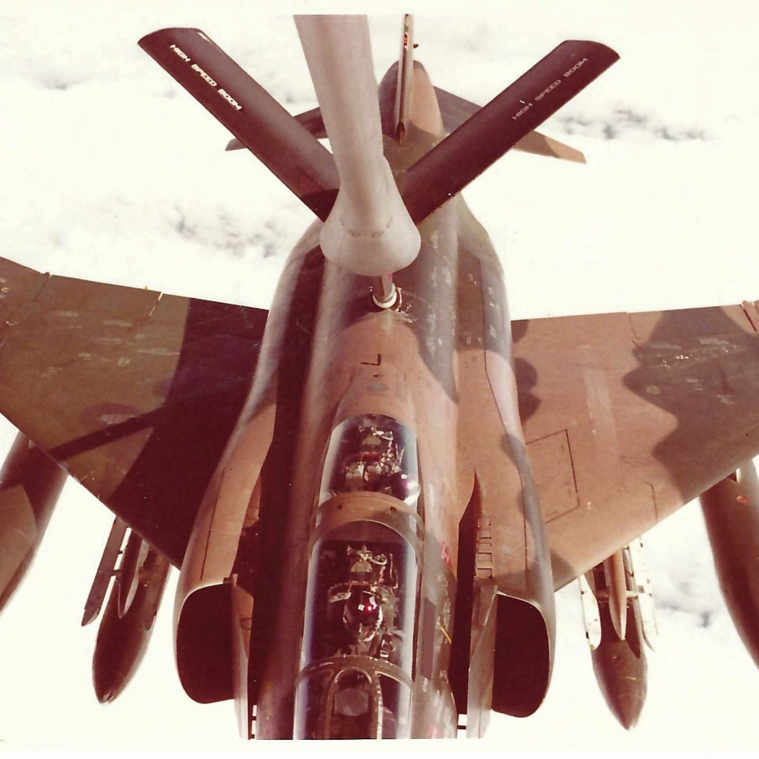 Fighter jet flying above clouds, showcasing its cockpit and weaponry during a mid-air operation.