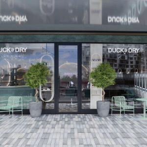 Stylish exterior of Duck & Dry at Battersea Power Station, featuring seating, greenery, and modern architectural design.