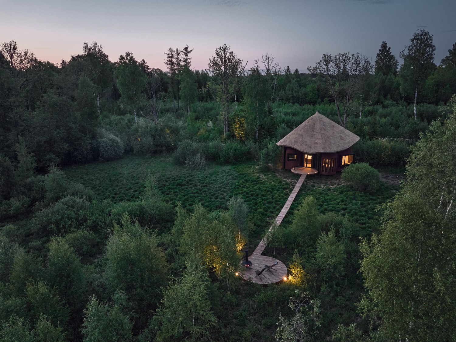 Aerial view of a traditional wooden villa surrounded by lush greenery and trees at dusk.
