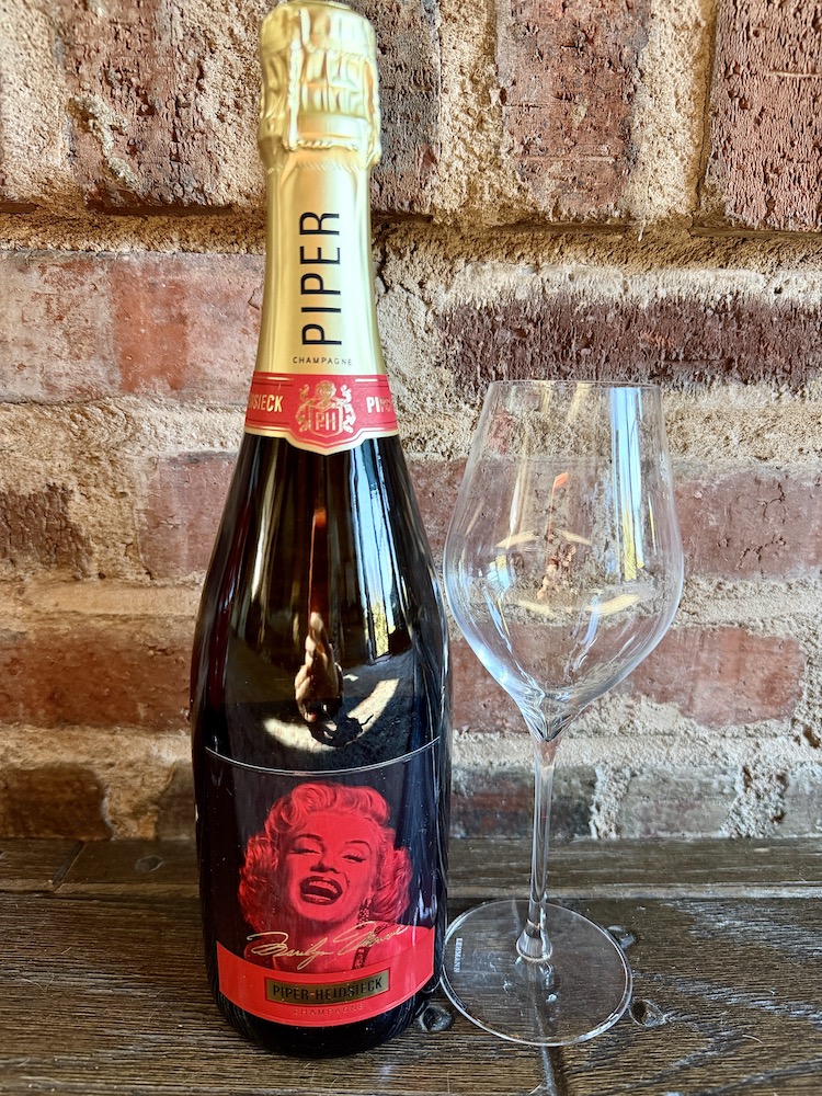 Piper-Heidsieck champagne bottle featuring Marilyn Monroe's iconic image, accompanied by a clear champagne glass.