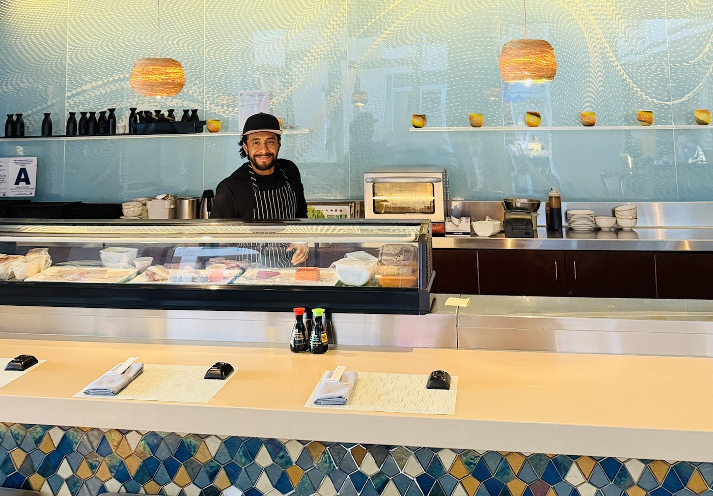 Sushi chef smiling behind the counter, featuring a display of sushi and various condiments at Renaissance Esmeralda Resort & Spa.