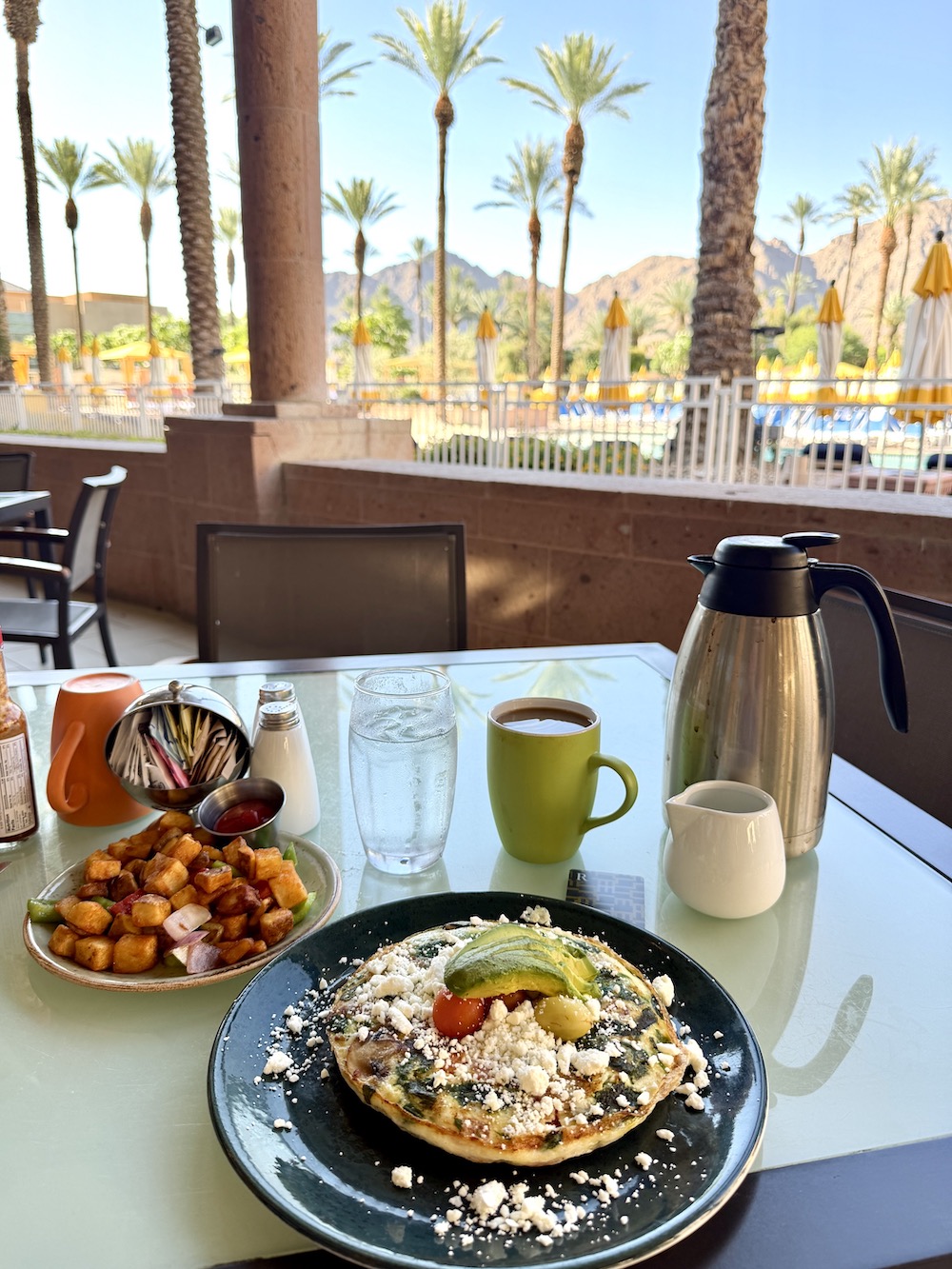 Breakfast spread featuring a frittata, seasoned potatoes, coffee, and a view of palm trees by the pool at Renaissance Esmeralda Resort.