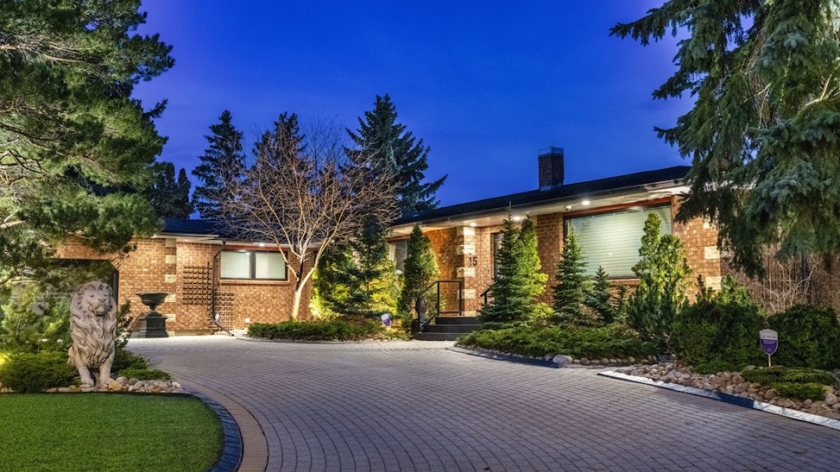 Spacious home exterior illuminated at night, surrounded by lush greenery and a circular driveway.