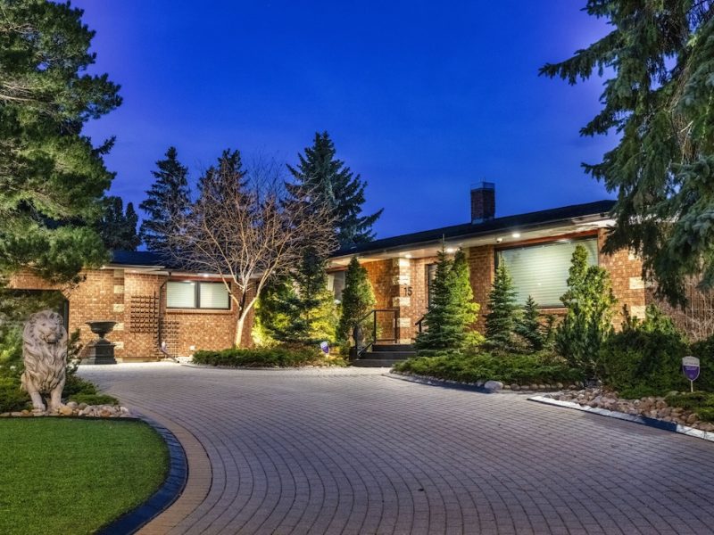 Spacious home exterior illuminated at night, surrounded by lush greenery and a circular driveway.
