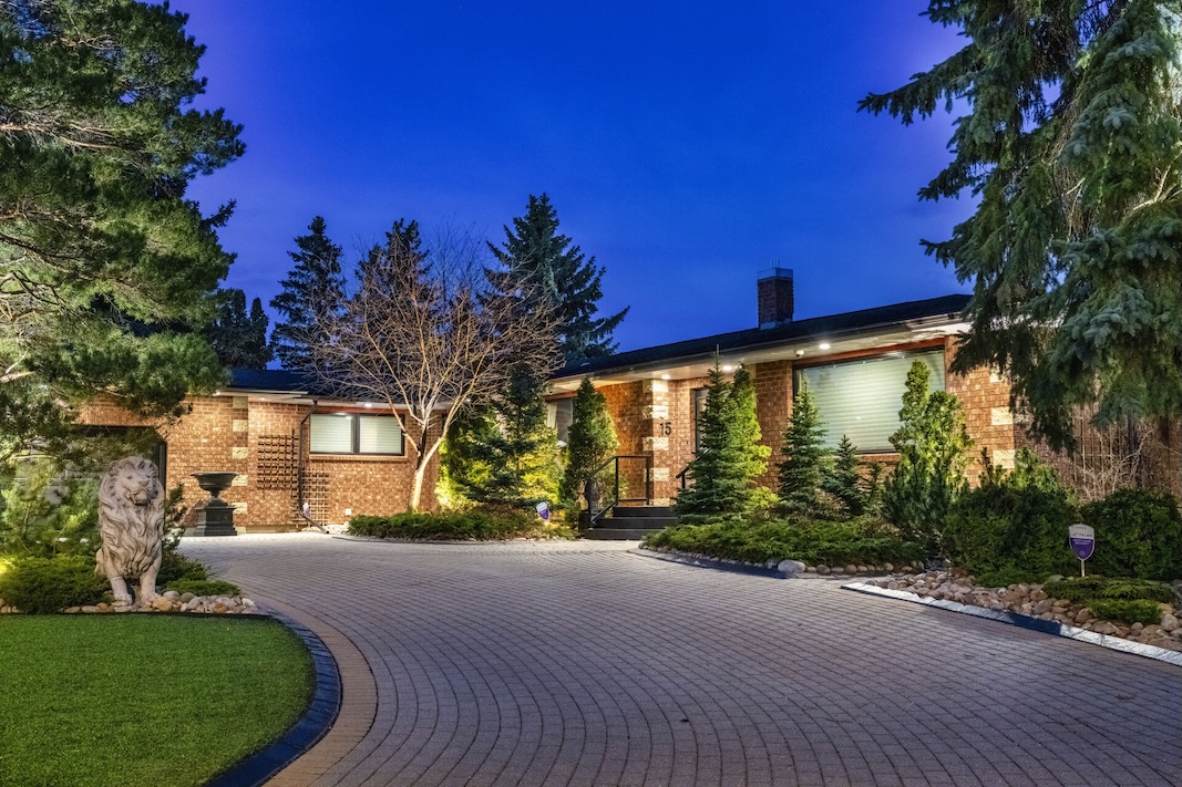 Spacious home exterior illuminated at night, surrounded by lush greenery and a circular driveway.