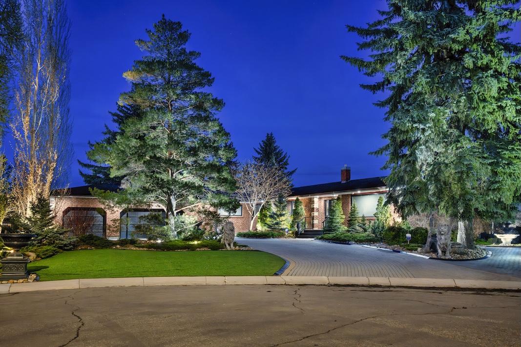 Elegant home surrounded by lush greenery under a night sky, showcasing beautifully landscaped grounds and inviting entrance.