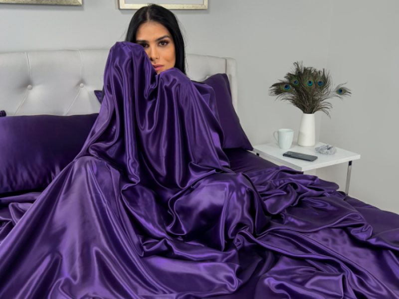 A model draped in luxurious plum silk bedding, showcasing elegance and comfort in a modern bedroom setting.