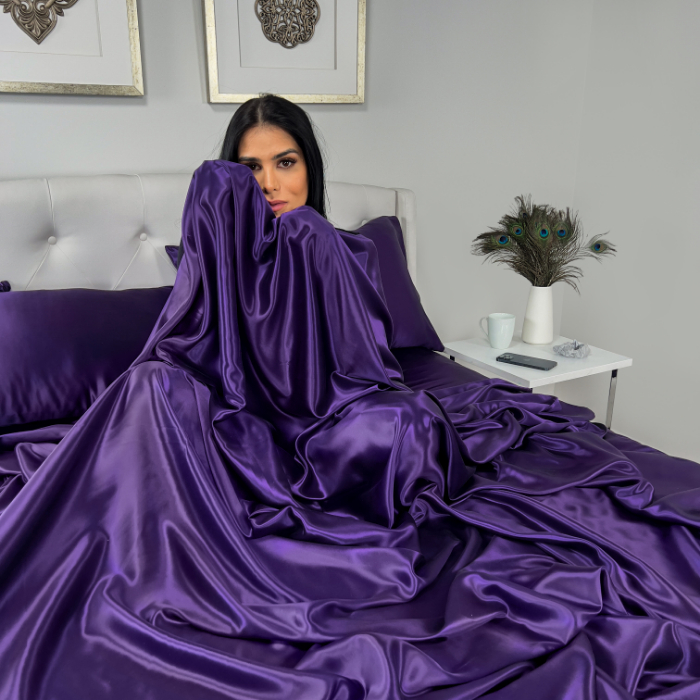 A model draped in luxurious plum silk bedding, showcasing elegance and comfort in a modern bedroom setting.