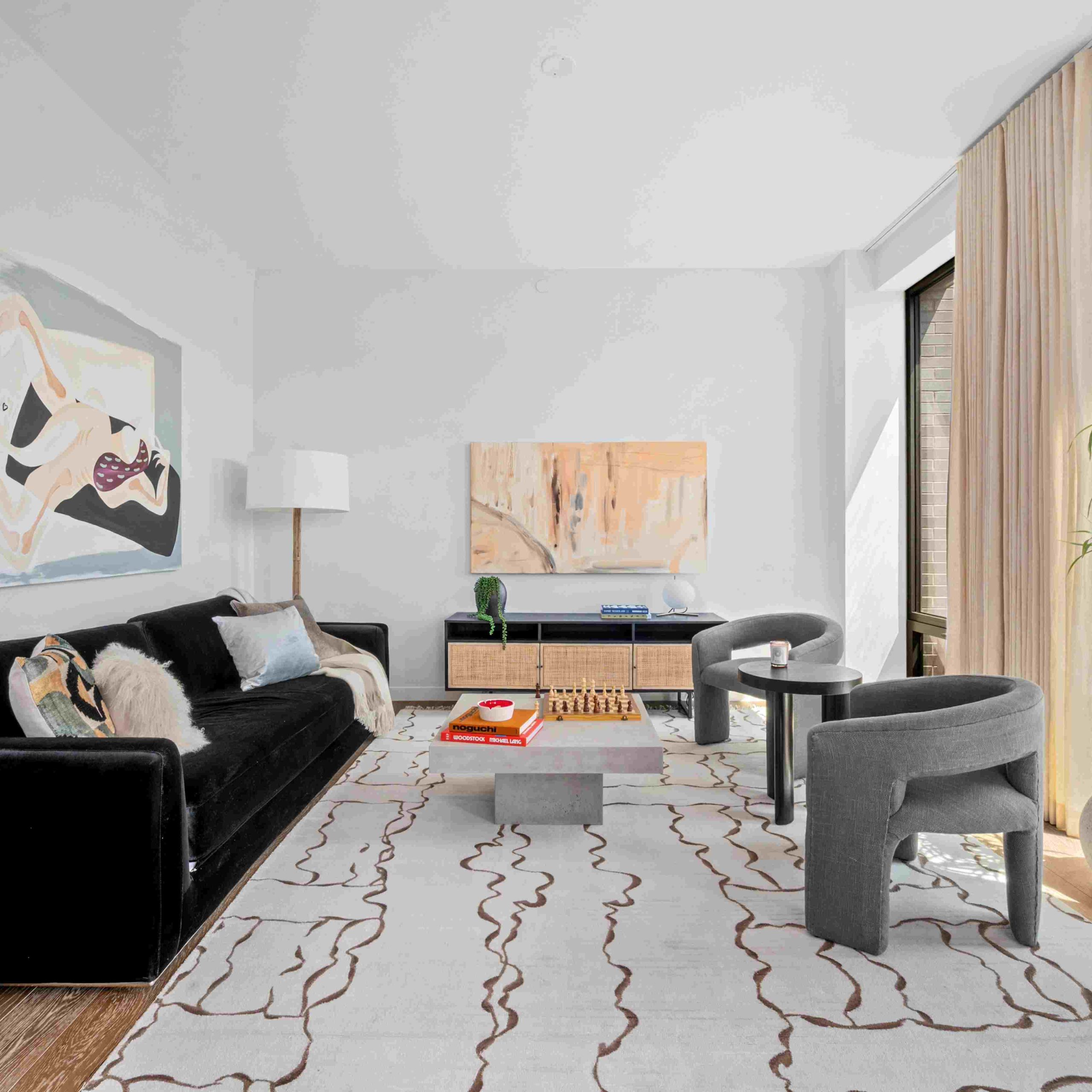Modern living room showcasing a black sofa, abstract artwork, and large windows with natural light, creating a stylish atmosphere.