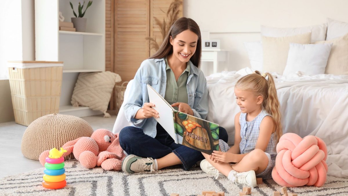 Aau pair reads a storybook with a young girl, surrounded by toys in a cozy living room setting.
