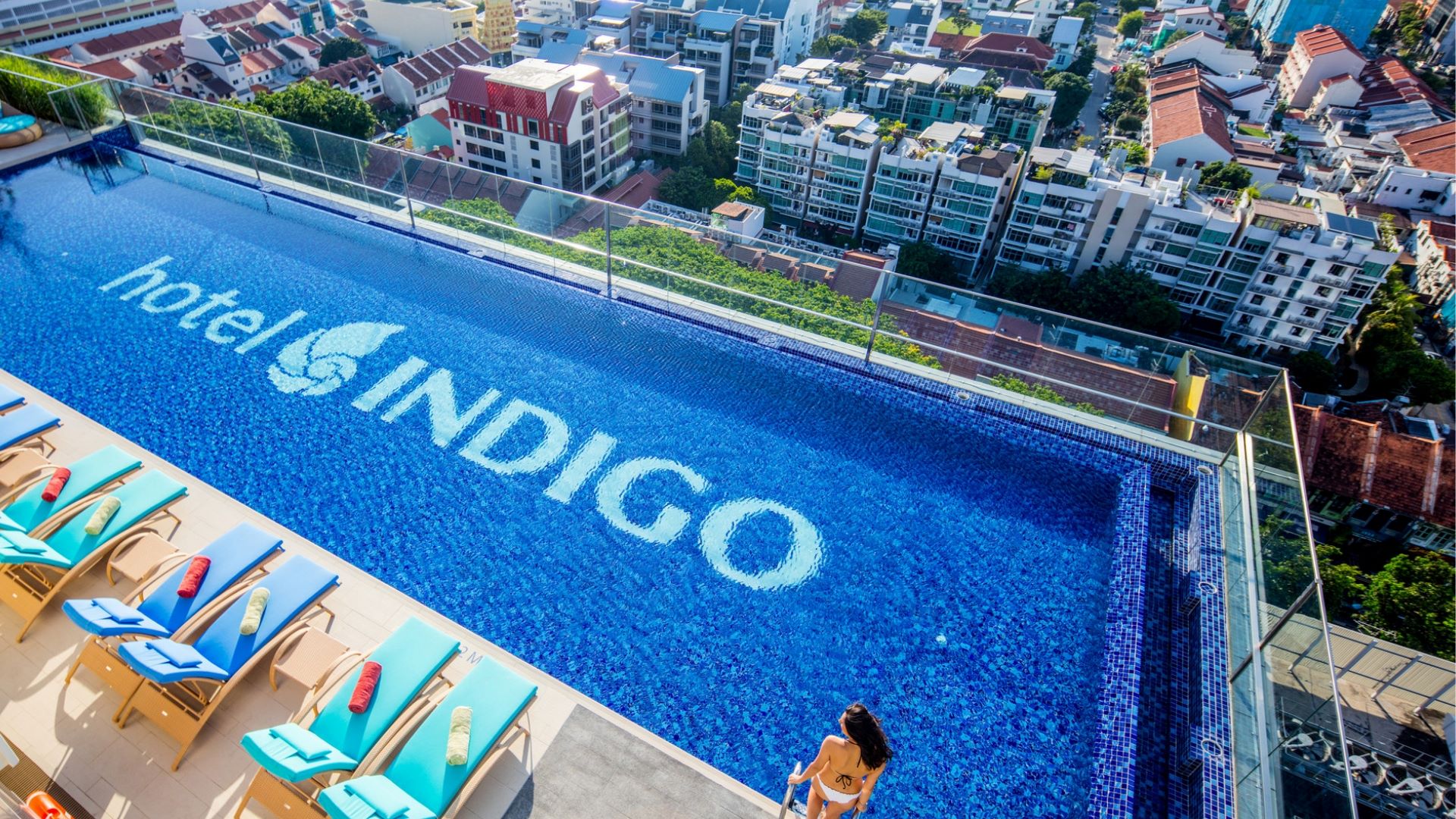 Rooftop infinity pool at Hotel Indigo with vibrant blue water and lounge chairs overlooking the city skyline.