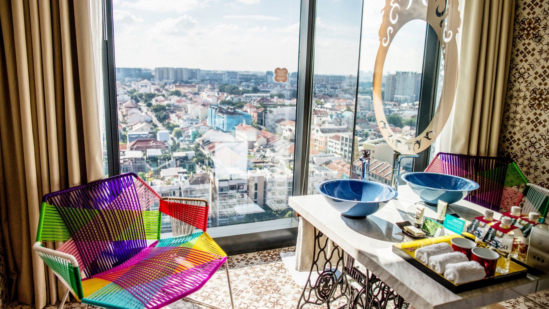 A colorful chair and modern sink set against a panoramic city view in a stylish hotel room.