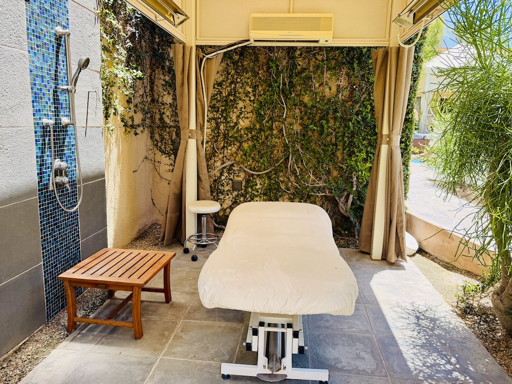 Outdoor treatment room with a massage table, shower, and greenery at Renaissance Esmeralda Resort & Spa.