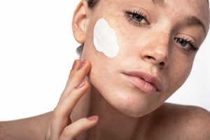 Model applying a cream to her face, showcasing beauty and skincare products for skin transformation.