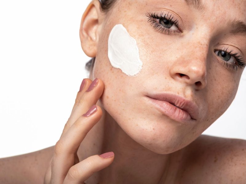 Model applying a cream to her face, showcasing beauty and skincare products for skin transformation.