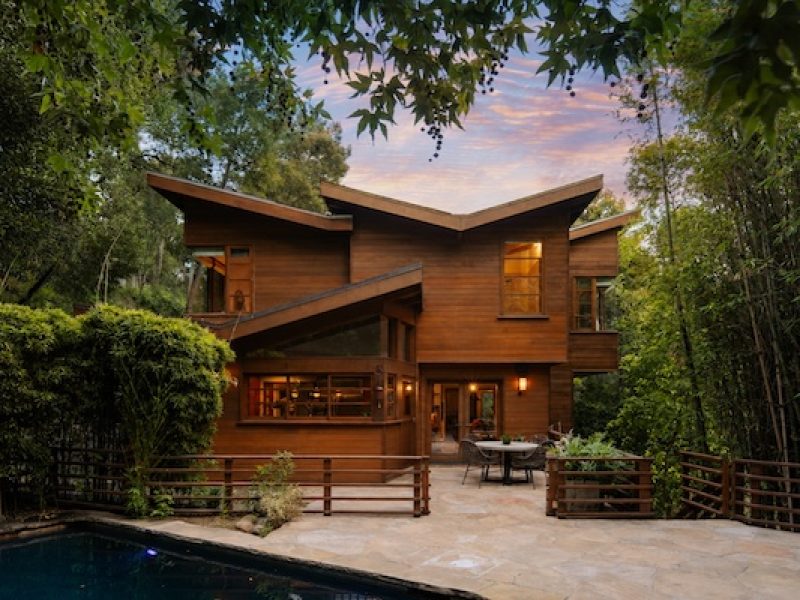 Modern wooden home surrounded by lush greenery and a pool, evoking a private countryside retreat atmosphere.
