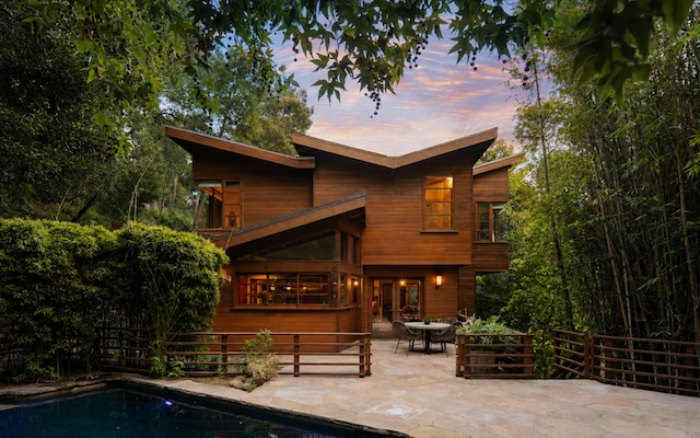 Modern wooden home surrounded by lush greenery and a pool, evoking a private countryside retreat atmosphere.
