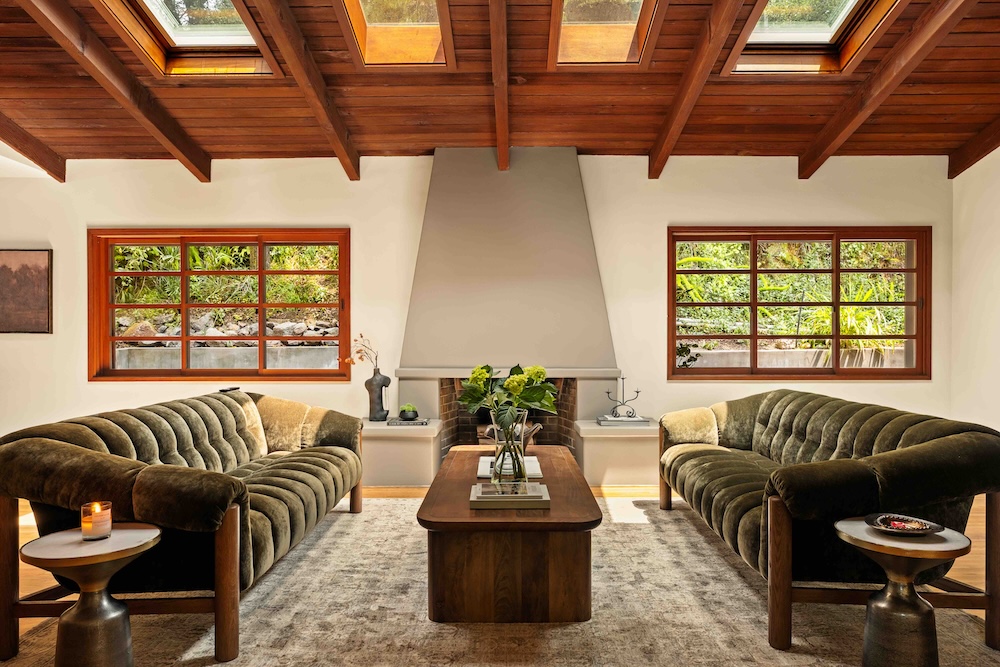 Stylish living room with a vaulted wooden ceiling, plush sofas, a coffee table, and large windows overlooking greenery.