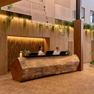 Reception area of an eco-luxury retreat featuring wooden decor, lush greenery, and staff at a natural log desk.