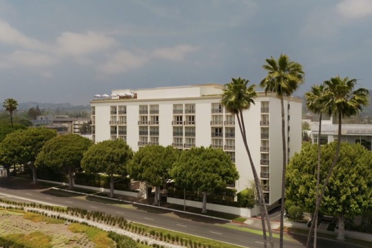 Beverly Hills hotel surrounded by lush trees, showcasing modern architecture against a clear sky.