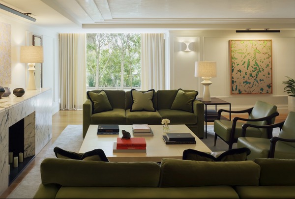 Modern living room featuring a green sofa set, marble fireplace, artwork on the wall, and abundant natural light from large windows.