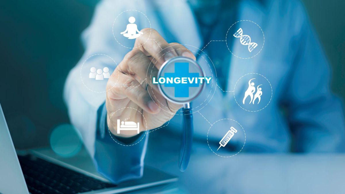 Hand reaching for a circular screen with the word "longevity," surrounded by health-related icons and a laptop in the background.