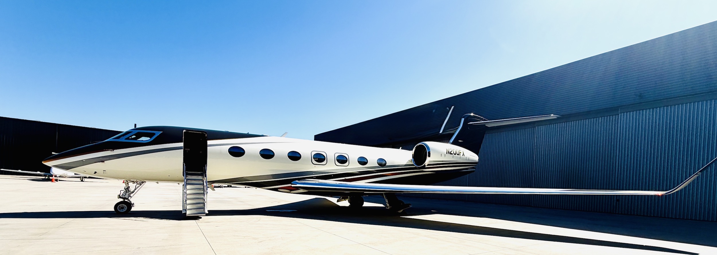 Luxury Gulfstream G500 jet with a sleek design and accessible stairs, parked against a clear blue sky.