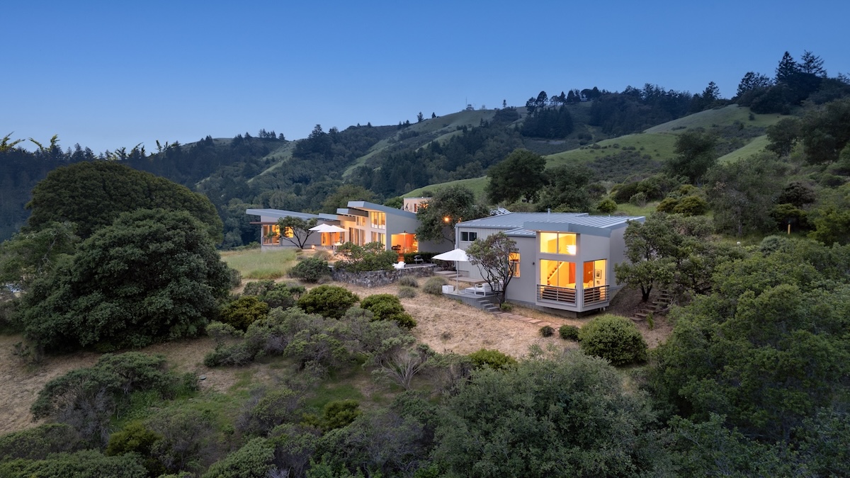 Modern retreat houses nestled in the hills of West Marin, surrounded by lush greenery and a clear evening sky.