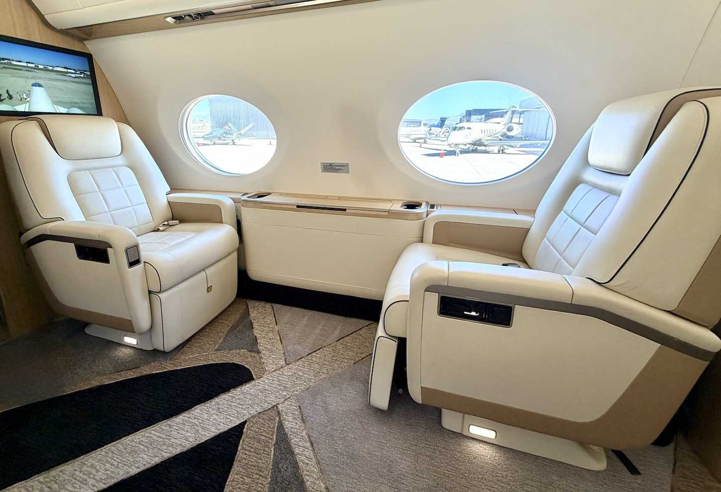 Luxurious seating area inside the Gulfstream G500 jet, featuring two plush chairs and large windows with an airport view.