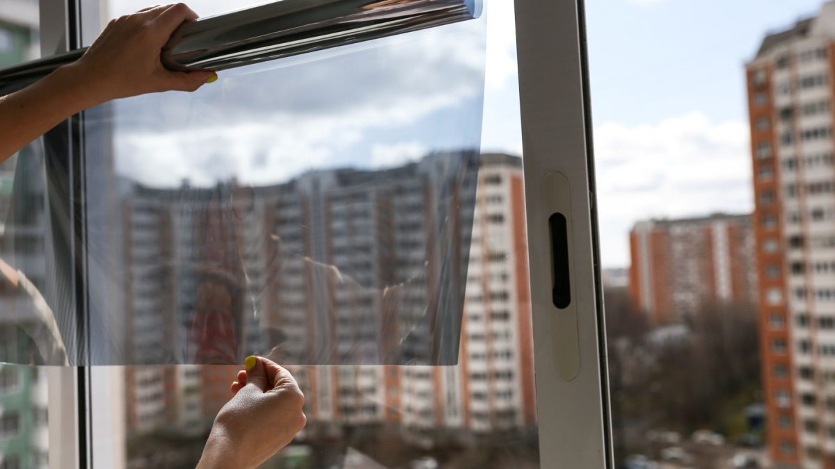Applying window tint film to reduce energy costs in a Phoenix home, with city buildings visible in the background.