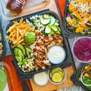 Colorful salad boxes featuring fresh vegetables, grilled chicken, and dressings, perfect for summer gatherings and celebrations.