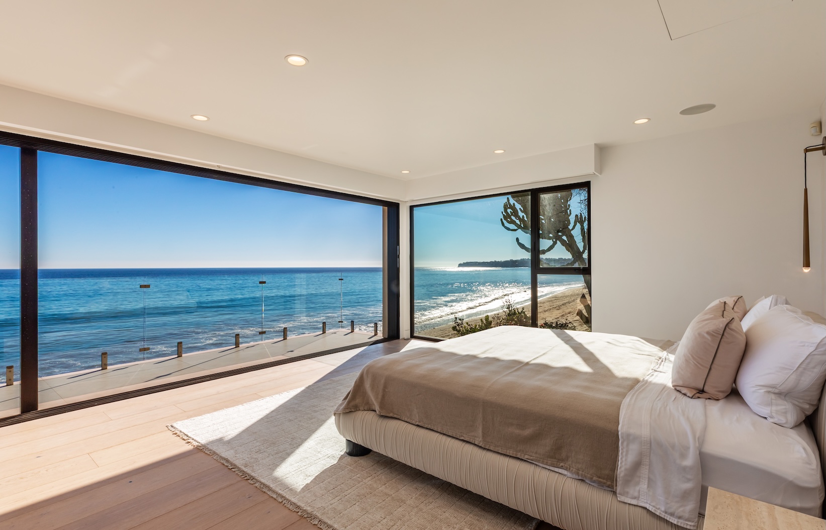 Bright, modern bedroom with large windows showcasing ocean views and beachfront in Malibu. Natural light illuminates the space.