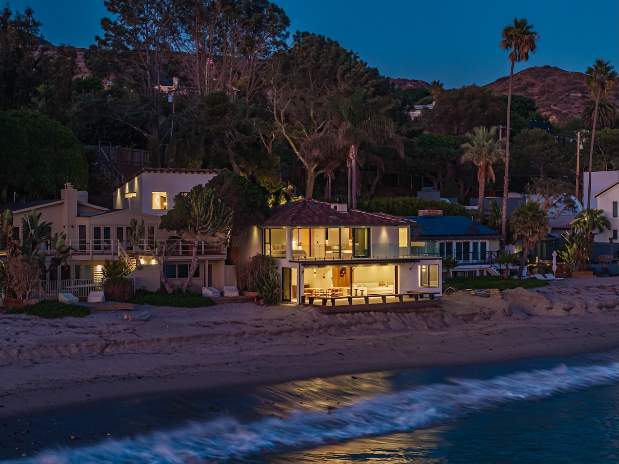 Elegant beachfront property at dusk, featuring modern architecture and surrounding palm trees along the Malibu coast.