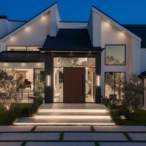 Modern home exterior featuring elegant lighting, landscaped lawn, and a striking entrance at dusk.