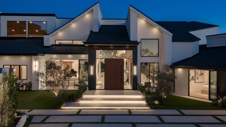 Modern home exterior featuring elegant lighting, landscaped lawn, and a striking entrance at dusk.