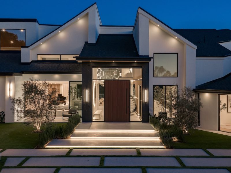 Modern home exterior featuring elegant lighting, landscaped lawn, and a striking entrance at dusk.