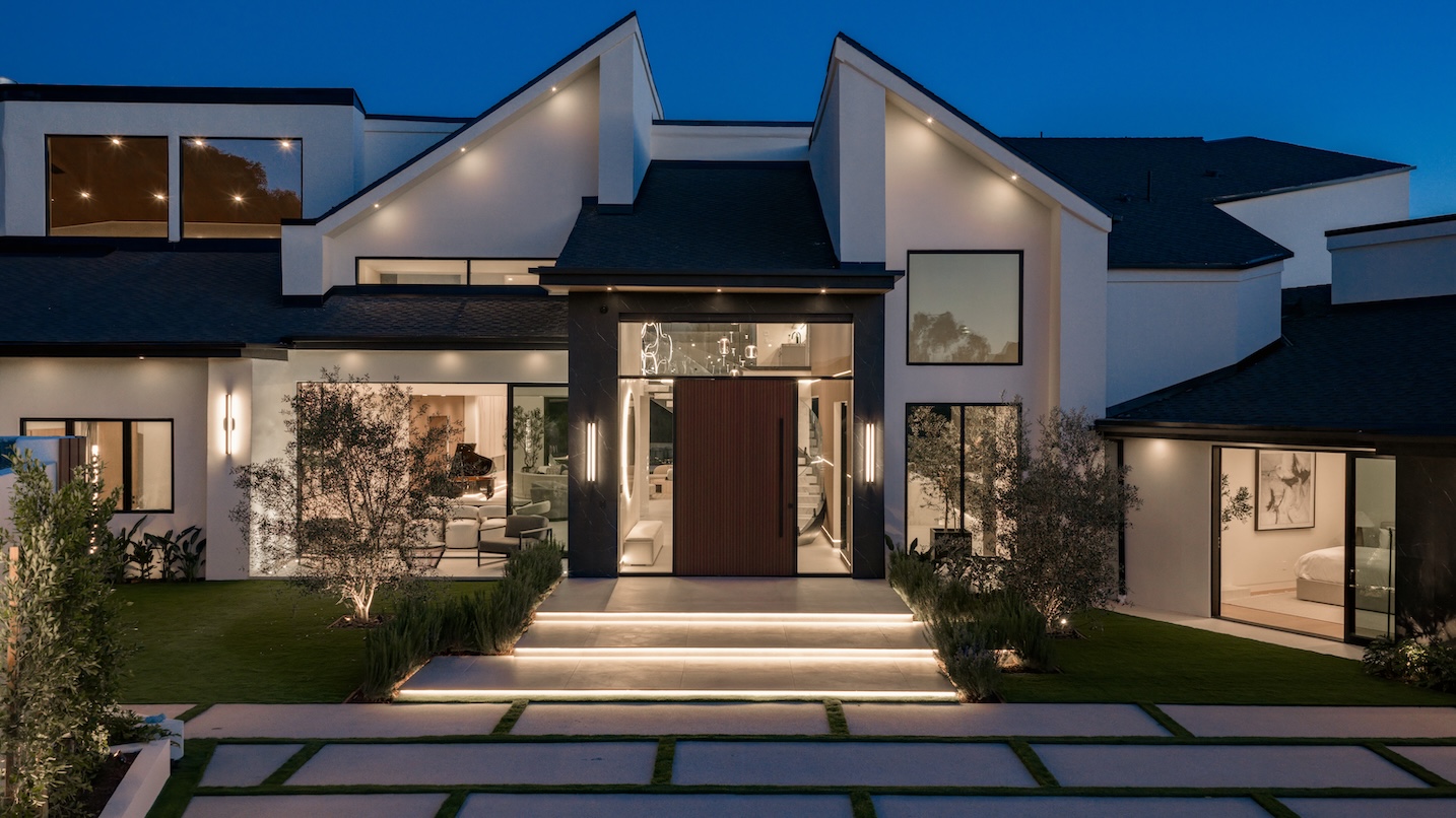 Modern home exterior featuring elegant lighting, landscaped lawn, and a striking entrance at dusk.