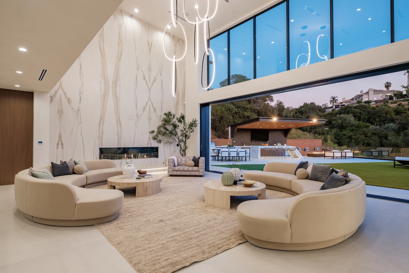 Luxurious modern living room featuring circular sofas, marble accent wall, and large windows with a view of the outdoor area.