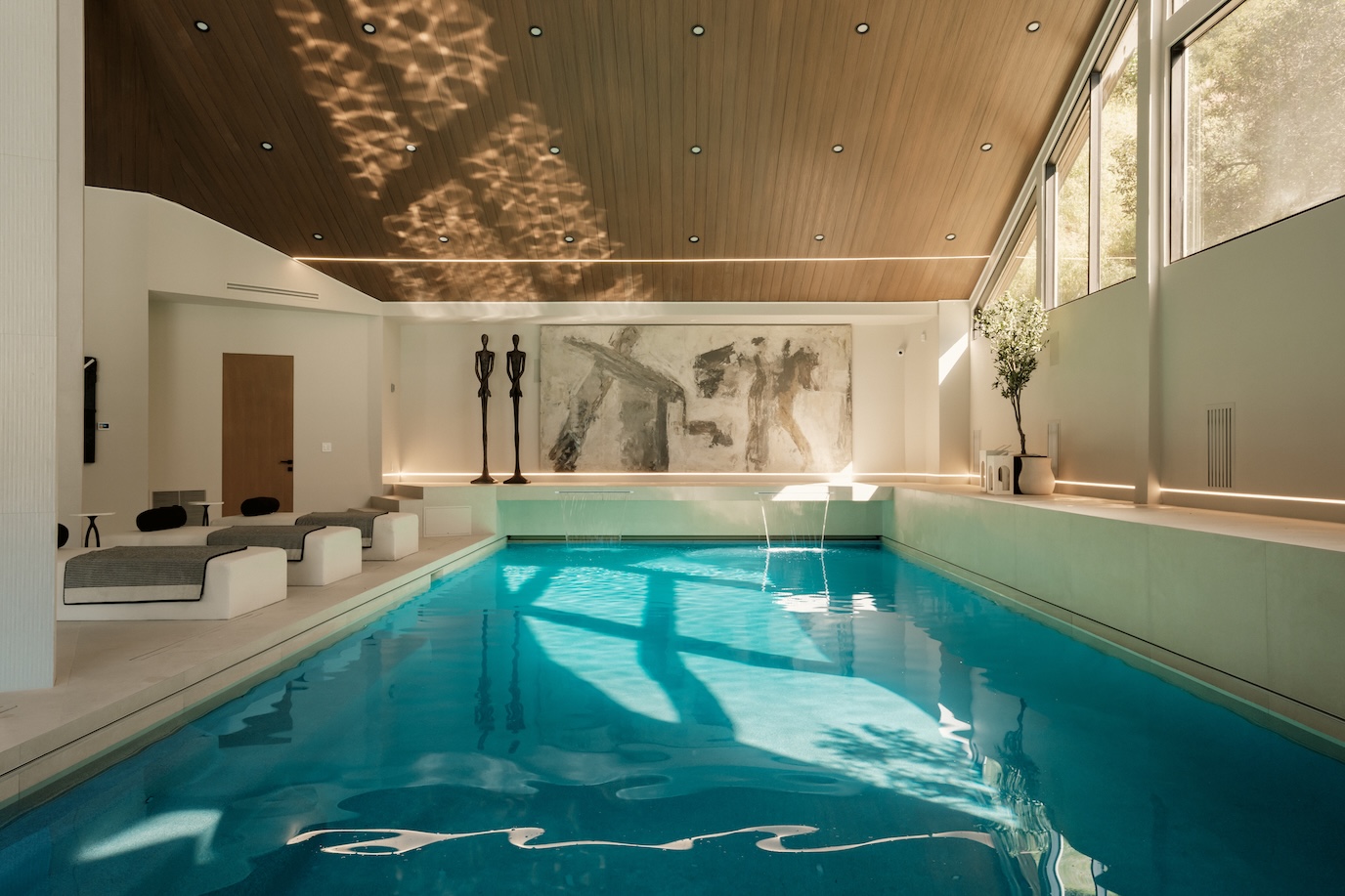 Contemporary indoor pool with modern seating, dramatic lighting, and an abstract mural in a spacious sanctuary setting.