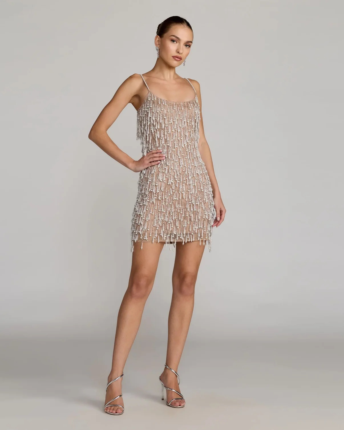 A model poses in a sparkling nude dress adorned with shimmering beads, exemplifying elegance and style for special occasions.