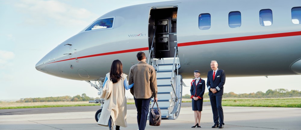 Passengers approach a VistaJet aircraft, greeted by crew members as they prepare to board for a luxurious travel experience.