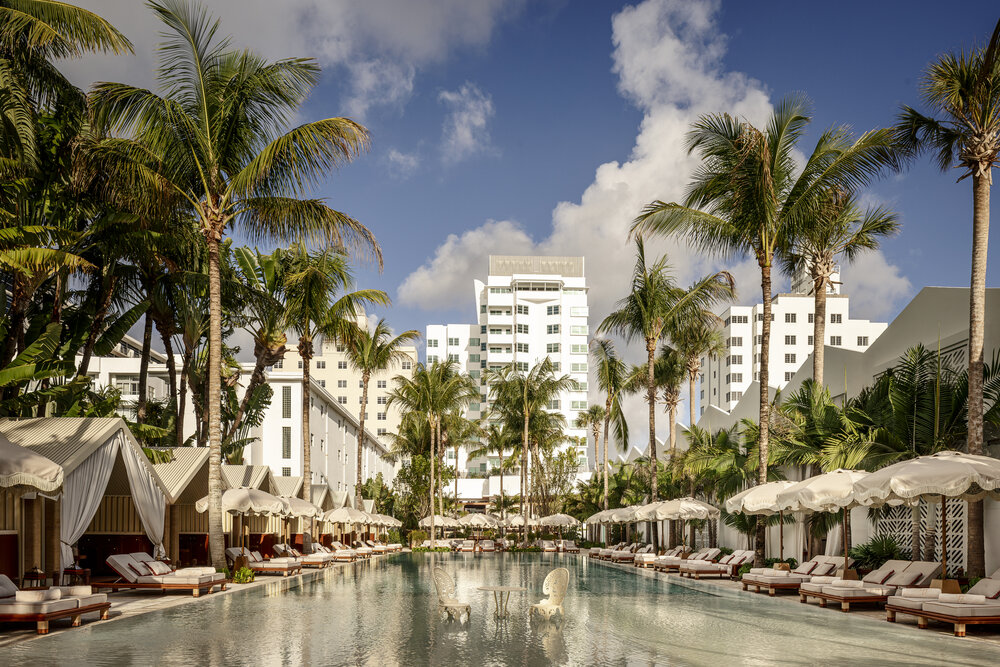 Lush palm trees surround the tranquil pool area at the historic Delano Miami Beach, featuring cabanas and elegant lounge chairs.