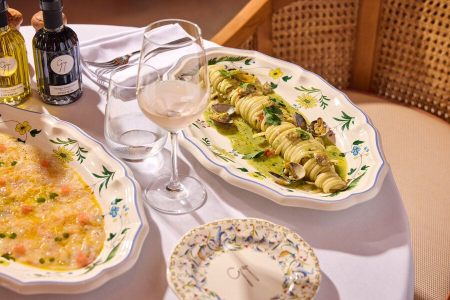 Linguine alle vongole served on a decorated platter, accompanied by a glass of white wine and bottles of olive oil and vinegar.