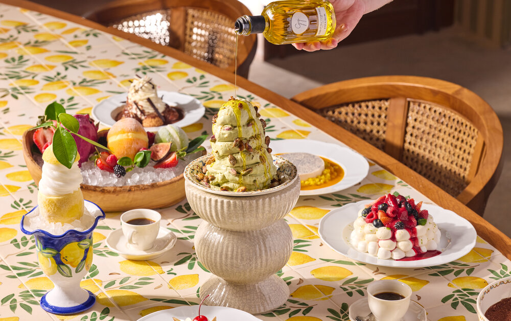 A beautifully arranged dessert table featuring pistachio gelato, fresh fruits, and various sweet treats on a lemon-patterned cloth.