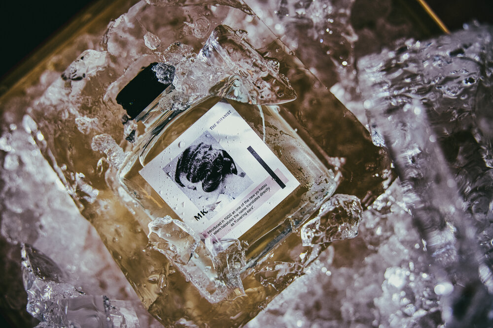 A bottle of fragrance surrounded by ice, featuring a minimalist label with artistic design elements.