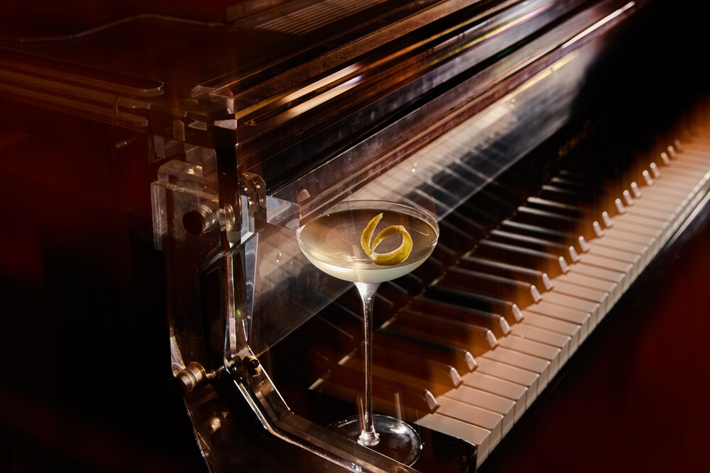 A cocktail garnished with lemon zest sits on a piano, blending culinary excellence with musical elegance at Delano Miami Beach.