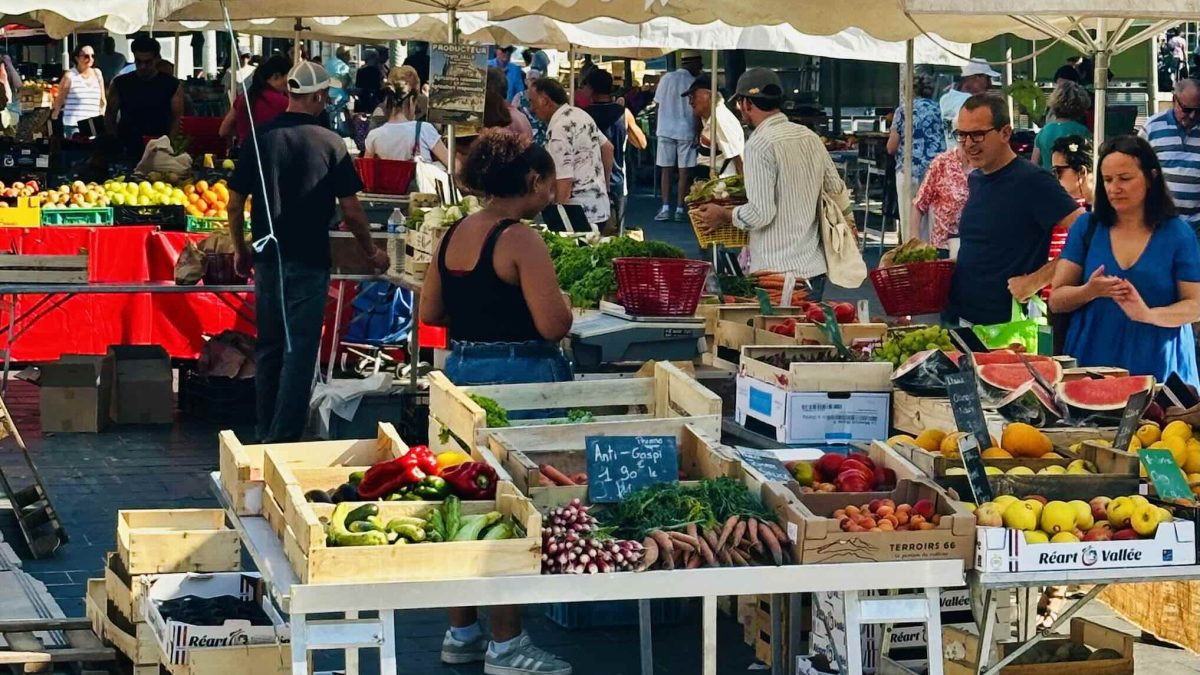Busy market scene showcasing vibrant fruits and vegetables at Nice's Marché de la Libération under sunny skies.