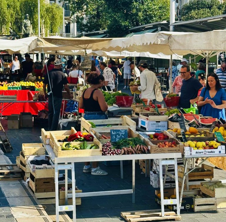 Busy market scene showcasing vibrant fruits and vegetables at Nice's Marché de la Libération under sunny skies.